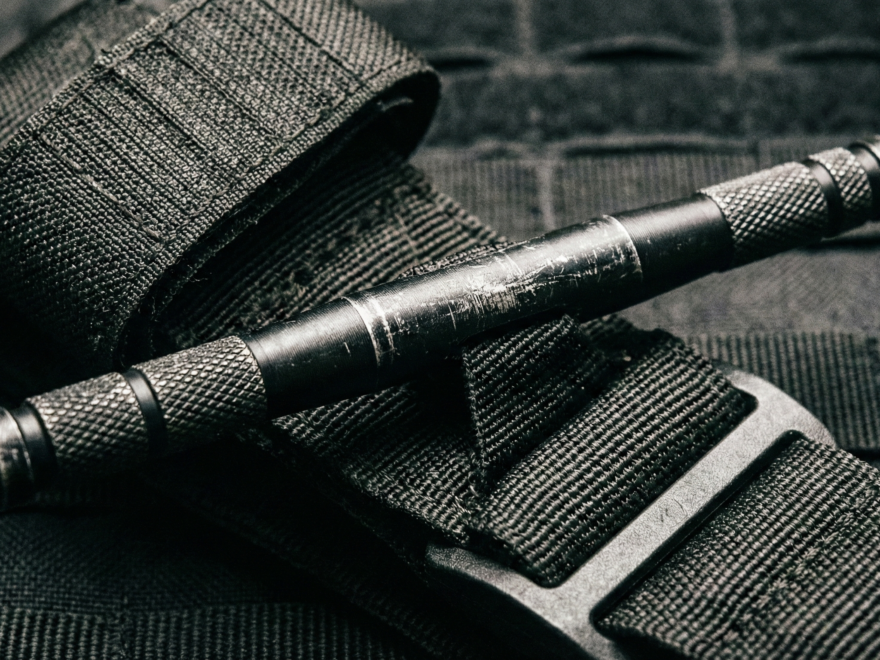 Close-up do torniquete tático nacional Desmodus T-APH, destacando sua haste de duralumínio inquebrável, projetada para uso extremo em APH tático e controle de hemorragias.